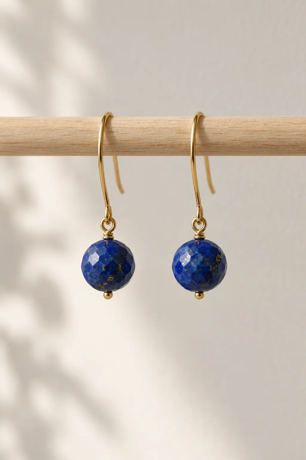 Illustration: zwei Ohrhänger aus Gold mit facettierten blauen Steinkugeln an einer Holzstange